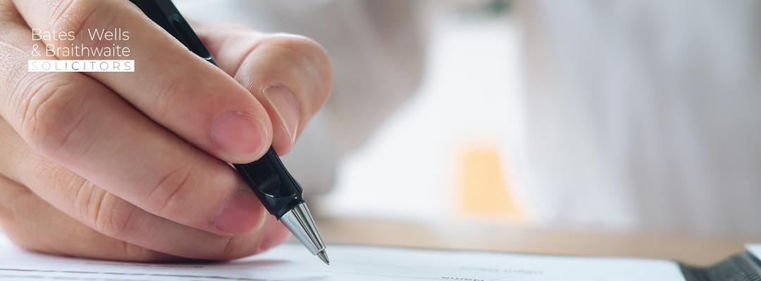 Close-up of a hand signing a document with a black pen; law firm logo visible in the top-left corner.